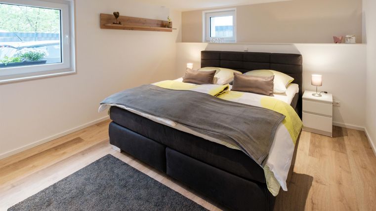 Ein modernes Schlafzimmer mit einem großen Doppelbett und einer neutralen Farbpalette. Die gemütliche Atmosphäre wird durch weiche Beleuchtung und einen hellen Holzboden ergänzt.