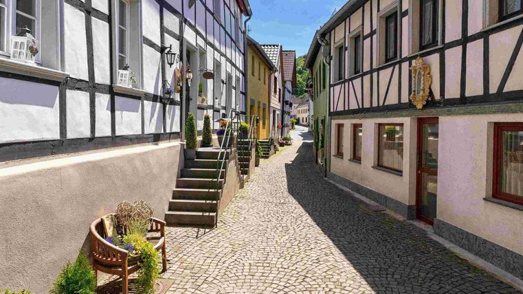 A picturesque street with timber-framed houses and cobblestone pavement. The surroundings are bright and inviting, with a clear blue sky.