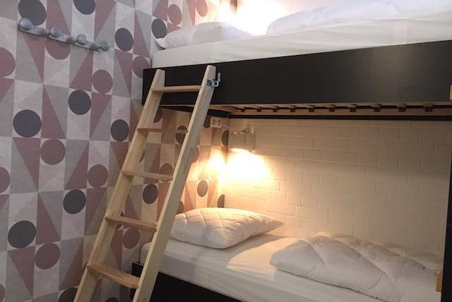 A cozy bedroom with a bunk bed and a wooden ladder. The walls are decorated with a modern, geometric pattern.