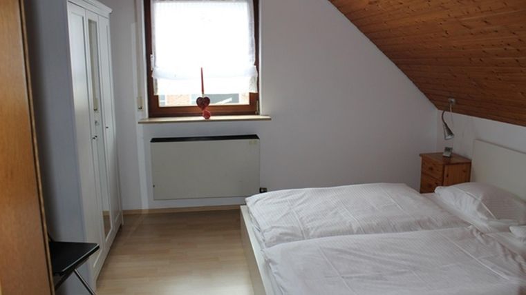 A simple bedroom with two single beds and a window. The walls are bright, and there is furniture in a wood look.