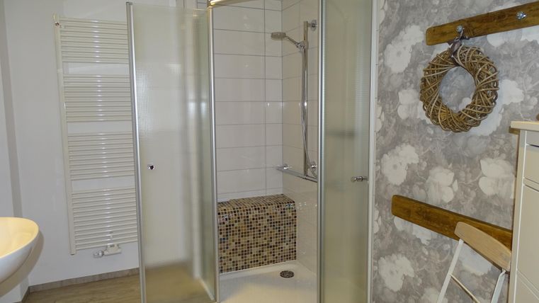 Een modern badkamer met een glazen douche en lichte tegels. Aan de muur hangt een decoratieve krans van natuurlijke materialen.