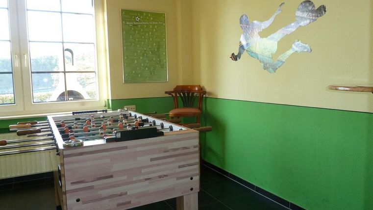 A play area with a foosball table and colorful wall design. A chair is in the corner, and a large window provides natural light.