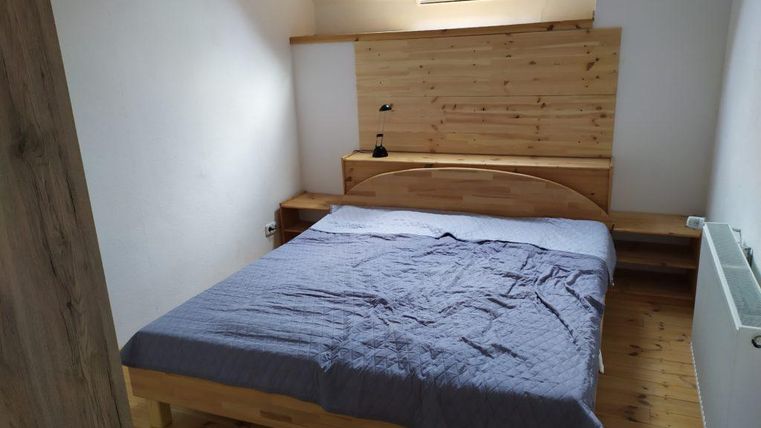 A simple bedroom with a wooden bed and a blue blanket. There is a window with a skylight and a wooden shelf wall.
