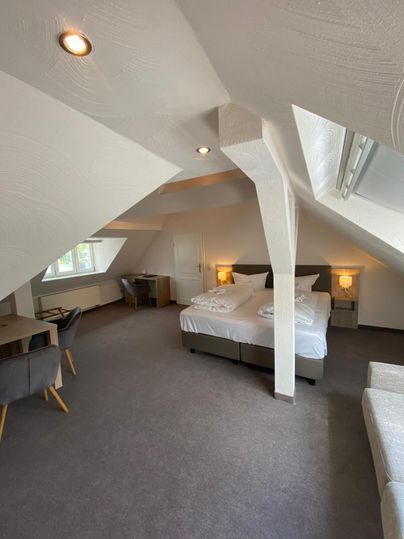 A cozy room in the attic with two beds, a desk, and a window. The walls are white and the lighting is pleasant.