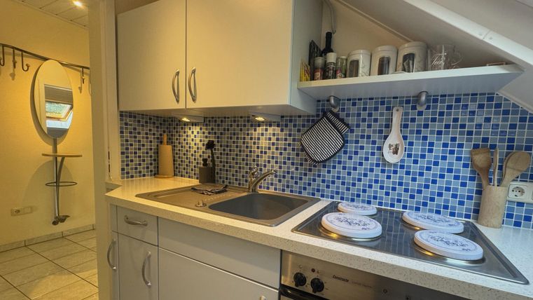 Een moderne keuken met witte kasten en blauwe tegels. Deze omvat een kookruimte met een fornuis en een gootsteen.