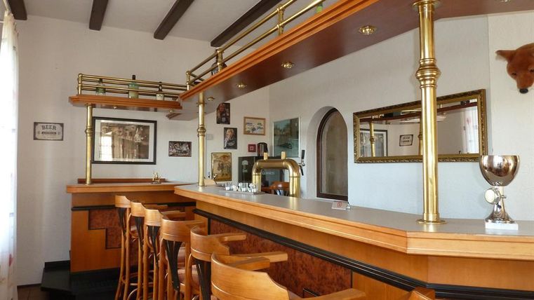 A cozy bar with wooden bar stools and an elegant bar counter. Pictures hang on the walls, and there is a trophy on the counter.