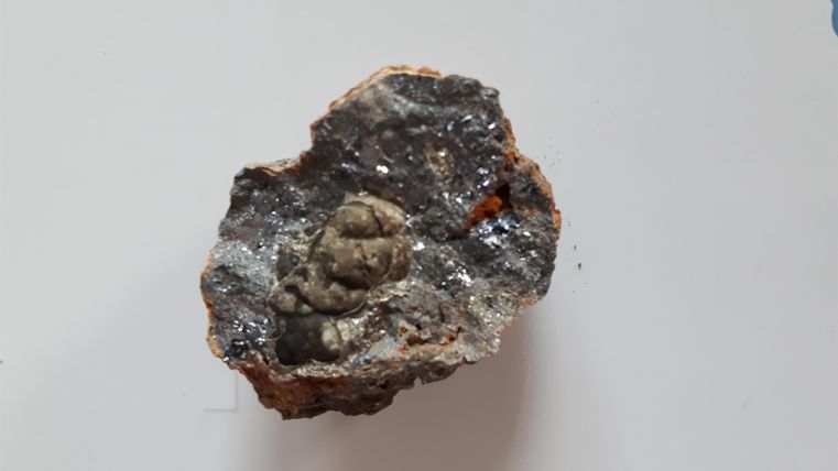 Ein Gesteinsstück mit einer kleinen, eingekapselten Figur im Inneren. Die Oberfläche ist rau und zeigt verschiedene mineralische Strukturen.