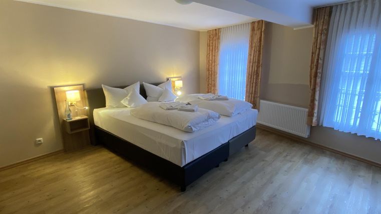 A cozy bedroom with a large double bed and bright curtains. The warm lights create an inviting atmosphere.
