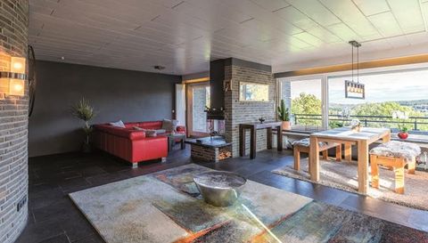 A modern living room with a red sofa and a large dining table. Large windows offer a view of nature.