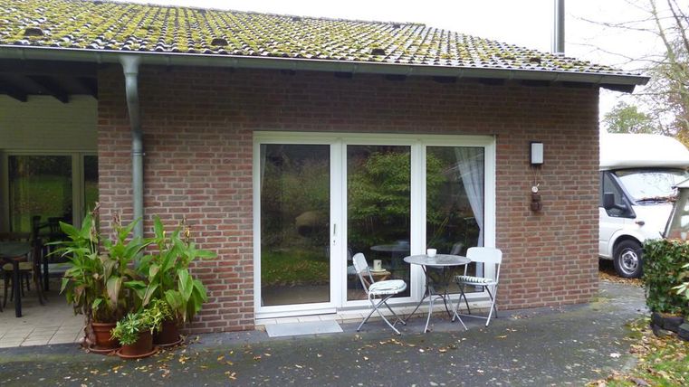 Een modern huis met een terras. Er is een kleine tafel met stoelen en enkele planten.