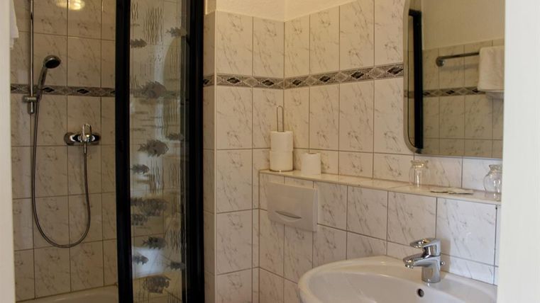 Een kleine badkamer met een douchecabine en een wastafel. De muren zijn betegeld met lichte tegels.