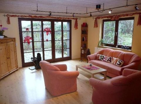 Een gezellige woonkamer met roze stoelen en een tafel in het midden. Grote ramen bieden uitzicht op de tuin.
