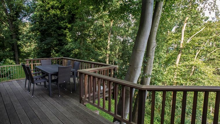 A cozy wooden terrace with a table and chairs, surrounded by trees. The view of the green nature creates a relaxing atmosphere.