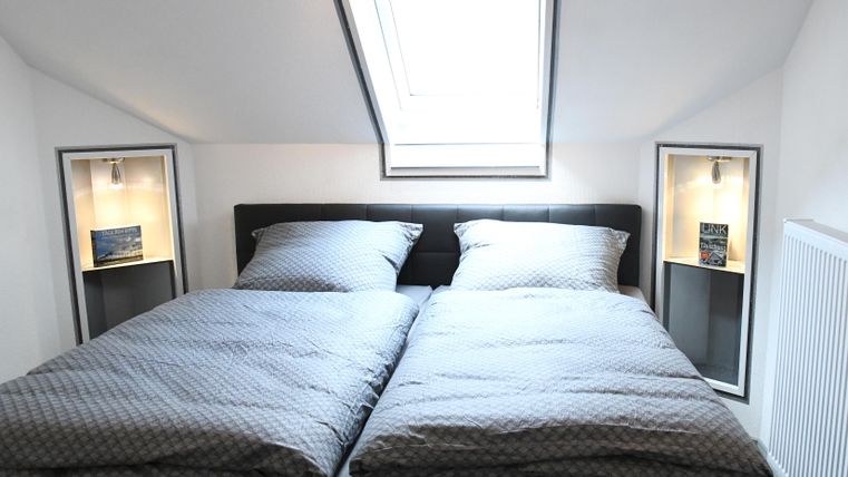 A bright bedroom with two combined beds. There are skylights and modern nightstands with lighting.