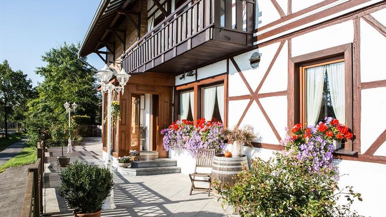 A charming half-timbered house with an inviting porch. Colorful flowers in pots and a cozy wooden chair create a friendly atmosphere.