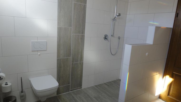 Een moderne badkamer met een douche en toilet. De muren zijn wit betegeld, en de vloer heeft grijze tegels.