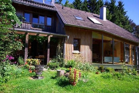 Een modern houten huis omringd door een weelderige tuin. De gevel heeft grote ramen en het gebied is goed verlicht.