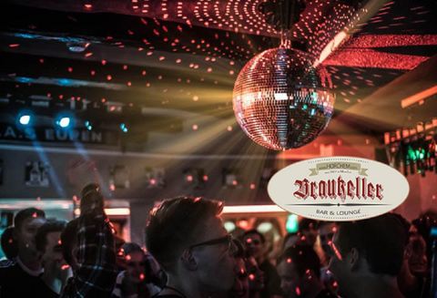 Een levendige bar met dansende mensen en een glinsterende discobal. Kleurrijke lichten creëren een feestelijke sfeer.