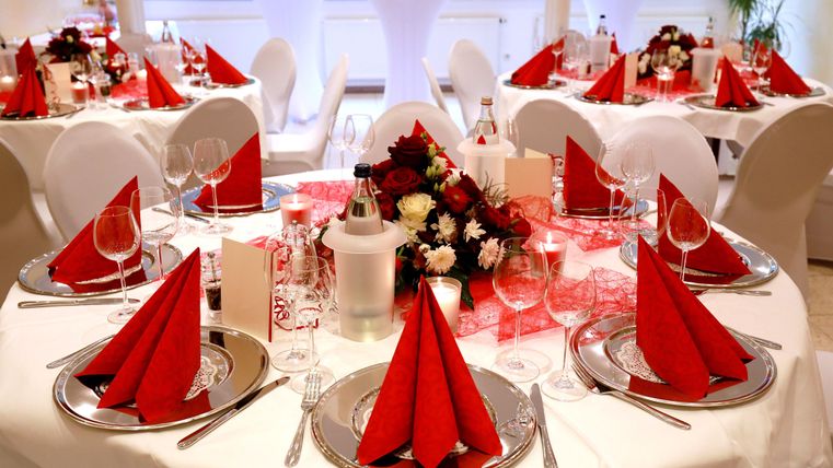 A festively decorated table with red napkins and elegant glasses. Flower arrangements and candles create an inviting atmosphere.