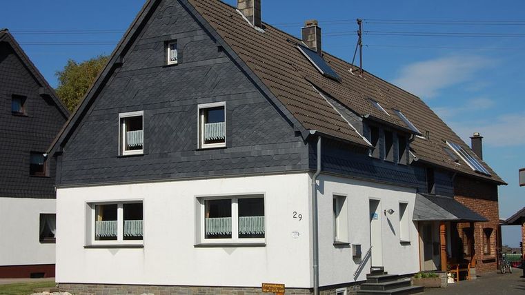 Een modern twee verdiepingen tellend huis met een combinatie van een zwarte en witte gevel. De ramen zijn licht en de dakpannen zijn bruin.