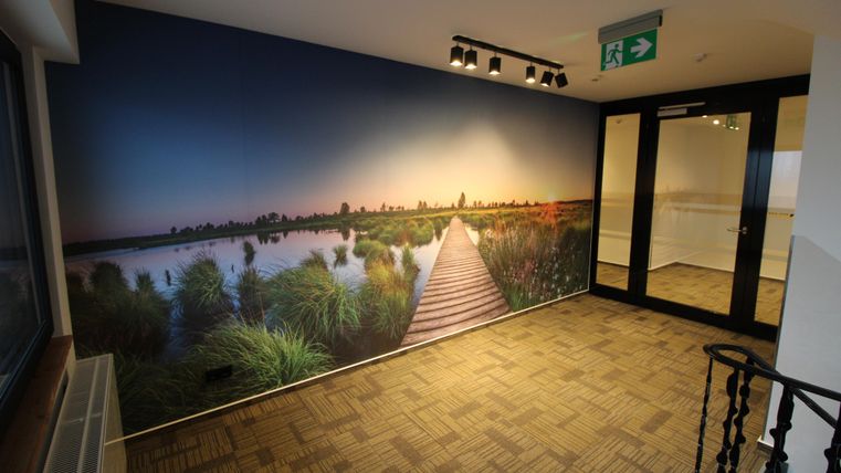 A bright room with a mural depicting a wooden bridge over a peaceful landscape. In the background, water and plants are visible.