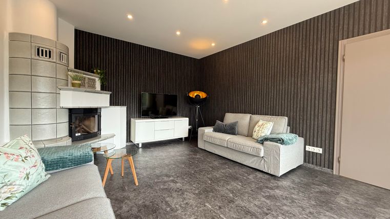 Een moderne woonkamer met comfortabele banken en een open haard. De muren zijn donker gestreept, en er is een tv-hoek.