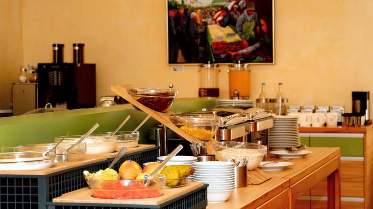 Ein reichhaltiges Frühstücksbuffet mit einer Auswahl an frischem Obst, Joghurt und Snacks. Im Hintergrund befindet sich ein farbenfrohes Gemälde.