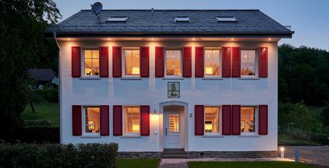 Een modern, twee verdieping tellend huis met witte muren en rode shutters. De ramen zijn verlicht en er is een smal pad naar de voordeur.