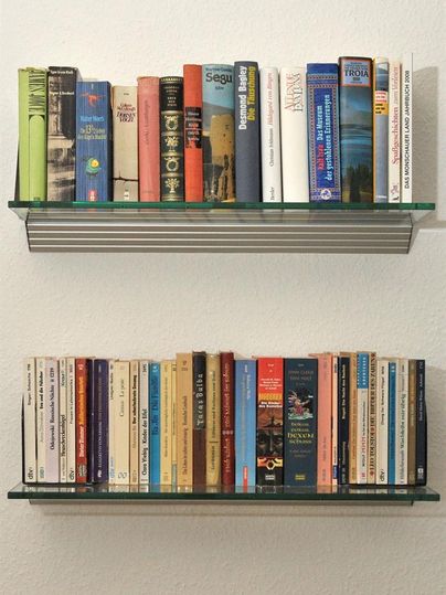 Twee boekenplanken met een verscheidenheid aan boeken in verschillende kleuren. De bovenste plank heeft grotere, gebonden boeken, terwijl de onderste plank voornamelijk paperbacks bevat.