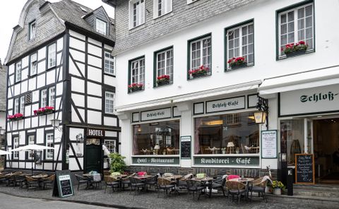 A picturesque cityscape with traditional houses and an inviting café. Tables and chairs are set up on the street, inviting a cozy stay.