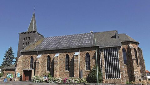 Een kerk met een steile toren en zonnepanelen op het dak. De gevel is van steen en de ramen zijn in gotische stijl ontworpen.