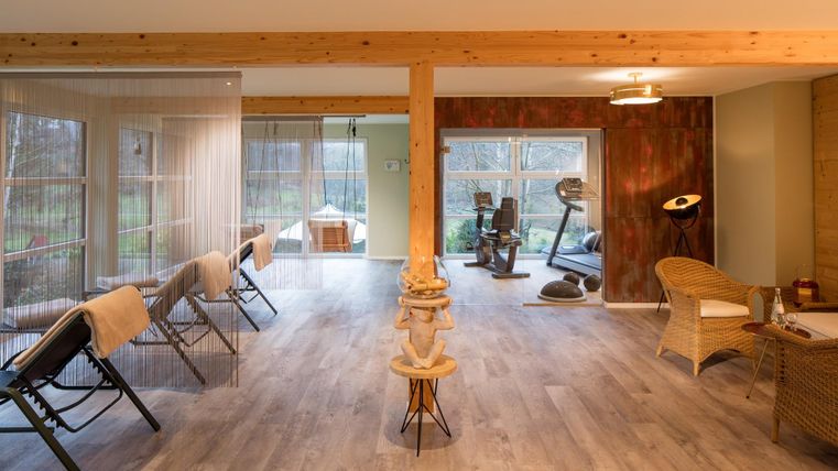 Een moderne ruimte met houtdetails en grote ramen. Er zijn ligstoelen en fitnessapparaten, evenals een gezellige ruimte om te ontspannen.