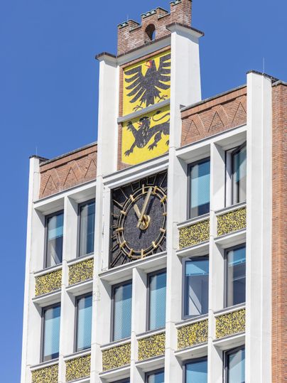 Ein historisches Gebäude mit einer großen Uhr und einem Wappen. Der Himmel ist klar und blau.