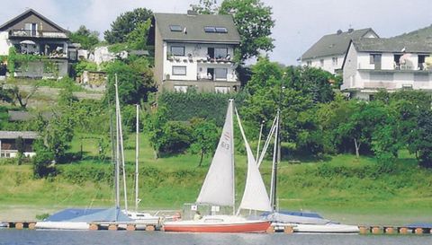 A calm water area with several sailboats in the foreground. In the background, green meadows and some houses can be seen.