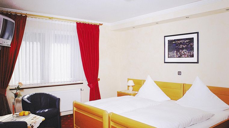 Een gezellig hotelkamer met twee bedden, een televisie en een fauteuil. Rode gordijnen en een muurschildering zorgen voor een uitnodigende sfeer.