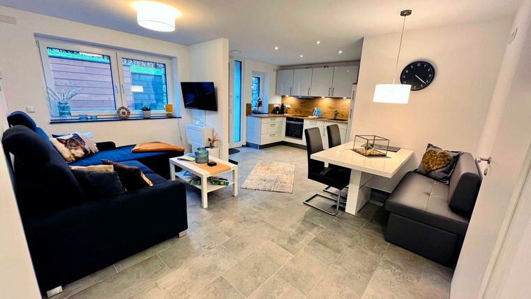 A modern kitchen-living room with a cozy sofa and a dining table. Large windows provide plenty of natural light.