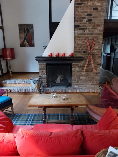 A cozy living room with a fireplace and red sofas. The room has a rustic atmosphere with wooden elements and modern wall decoration.
