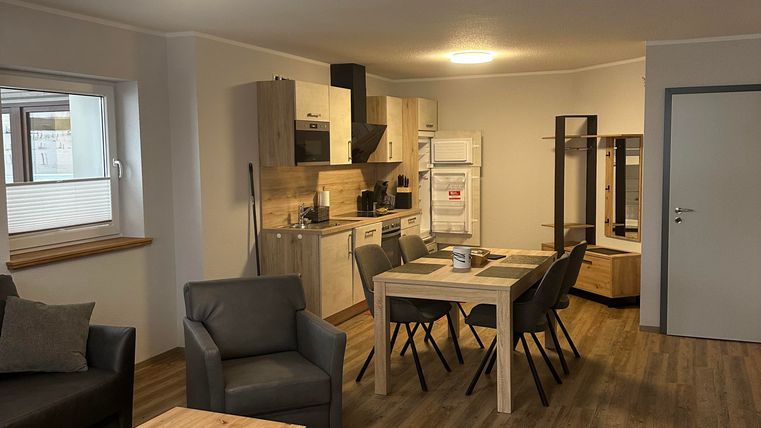 A modern apartment with an open kitchen and a dining area. The space is bright and cheerful, with wooden flooring and cozy furniture.