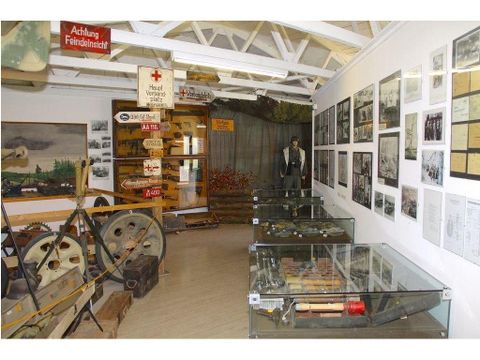 A museum with historical artifacts, including tools and photographs on the walls. In the center stands a statue, surrounded by display cases with various exhibits.