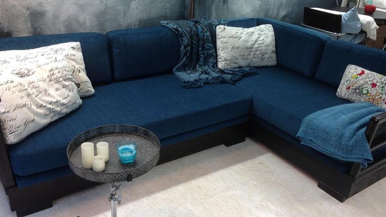 Een comfortabele blauwe bank met decoratieve kussens en een deken. Naast de bank staat een kleine tafel met kaarsen.