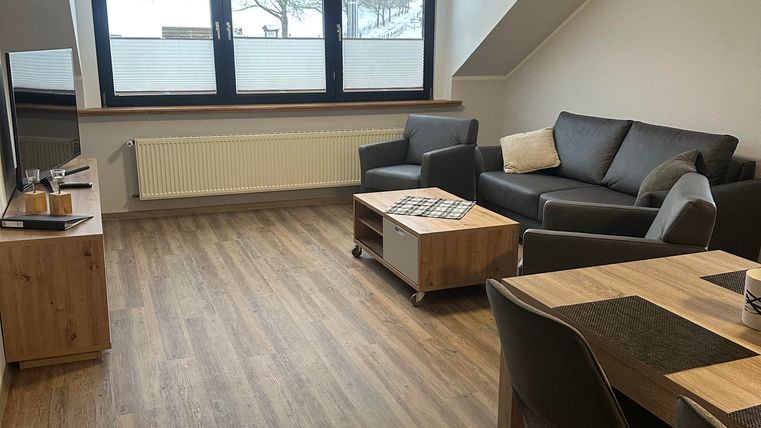 A modern living room with a gray sofa and a wooden coffee table. Large windows provide plenty of light and a view outside.