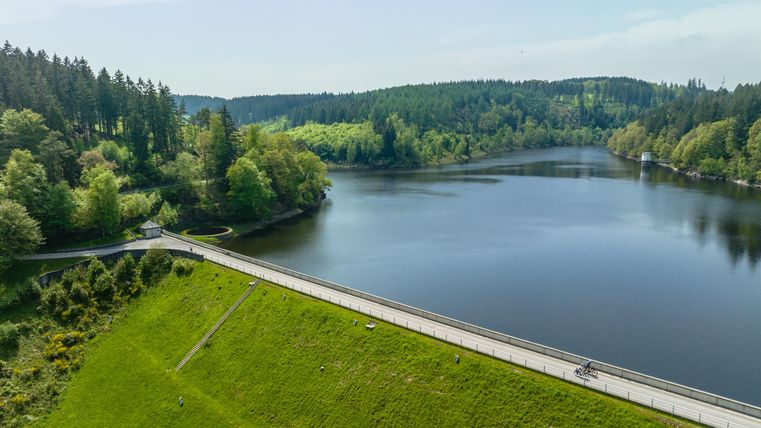 Een rustige meer omgeven door groene bossen en een mooi landschap. Een fietser rijdt langs een pad langs het water.