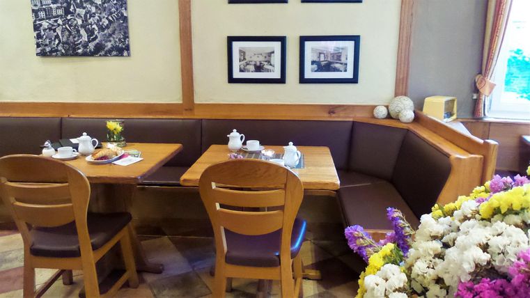 Een gezellig café met houten meubels en een koffieservice op een tafel. Aan de muur hangen schilderijen, en een boeket bloemen staat op de voorgrond.