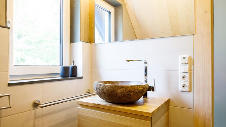 A modern bathroom with wooden details and a round sink. The window provides plenty of natural light.