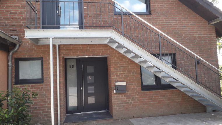 A modern building with an entrance and a metal staircase. The entrance is designed with a dark door and windows.