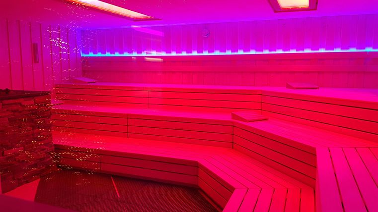 A modern wellness area with red and blue lights. The wooden seats are arranged in a stylish design.