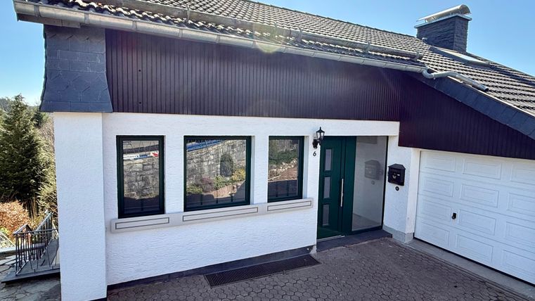 Een modern eengezinswoning met een groen aangelegde ingang. De gevel is licht geschilderd en heeft grote ramen.