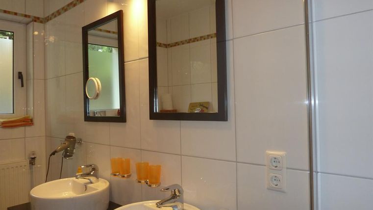 A modern bathroom with two sinks and large mirrors. The walls are brightly tiled, giving the room a clean atmosphere.