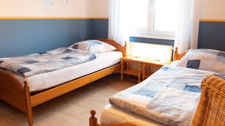 A simple room with two beds, bright walls, and a window. There is a small bedside lamp and a cozy atmosphere.