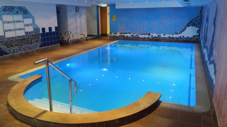 An elegant indoor pool with clear water and fluffy loungers. The walls are colorfully decorated with beautiful paintings.